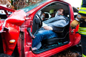 Accident - victim in a crashed vehicle, she receives first aid from firefighters